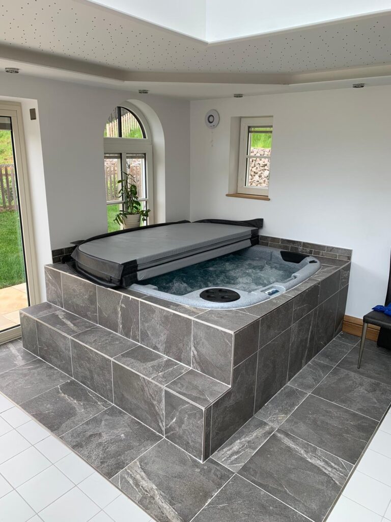 a grey tiled indoor with a square hot tub pool and a grey thermal co